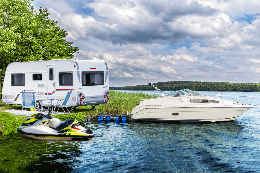 Camper, boat, and jet ski by lake.